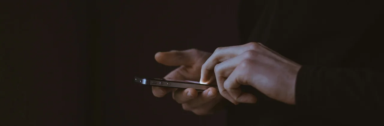 Un par de manos usando un teléfono casi a oscuras, con el borde de la pantalla iluminado
