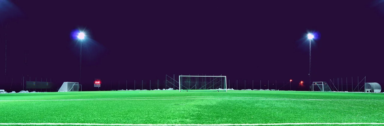 Cancha de fútbol iluminada por focos bajo un cielo nocturno violeta