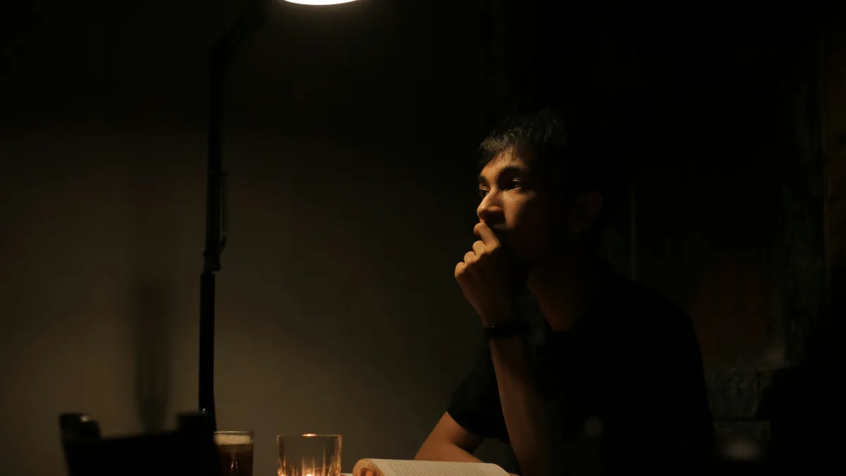 Persona sentada sola frente a una mesa en una habitación con poca luz, pensando